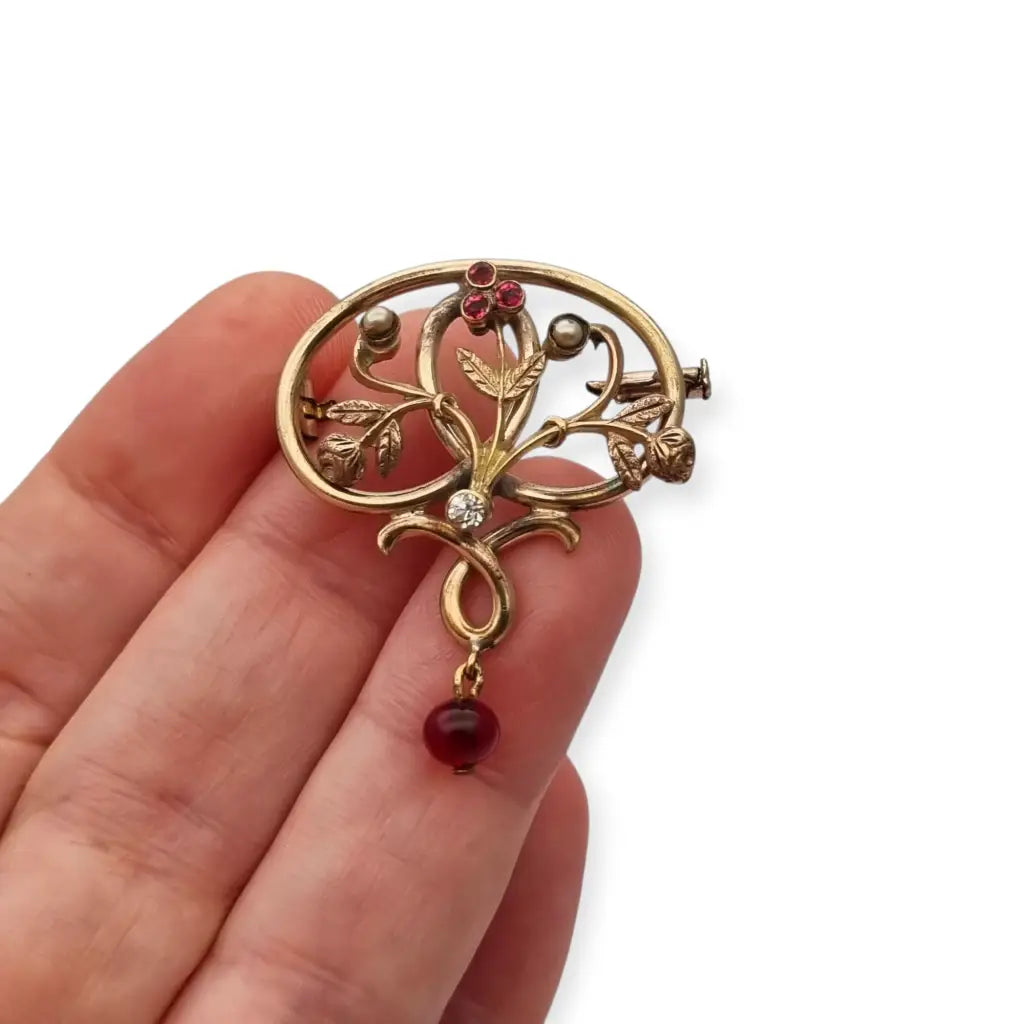 Broche Art Nouveau dorado con flor calada perlas y granates Circa 1900.