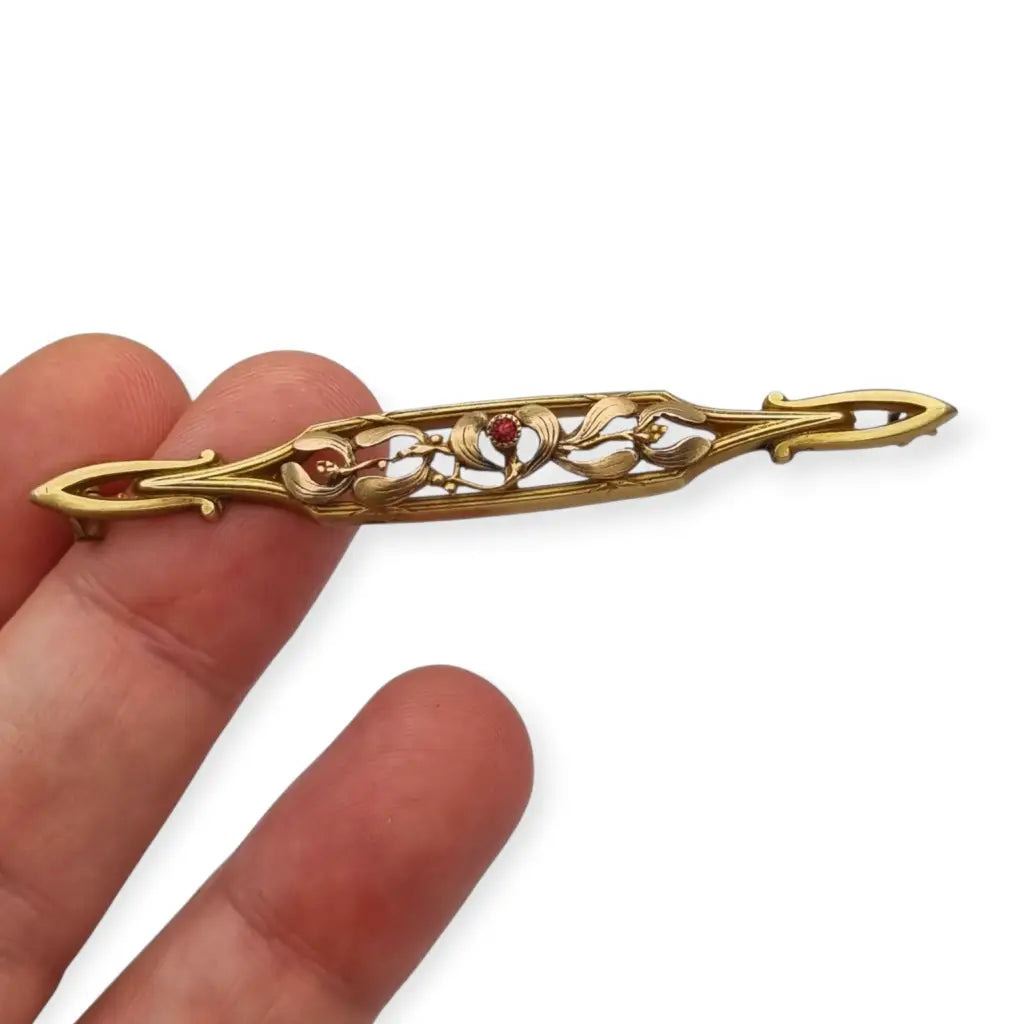 Broche Art Nouveau de Oria en oro laminado con flor calada y cristal rojo Circa