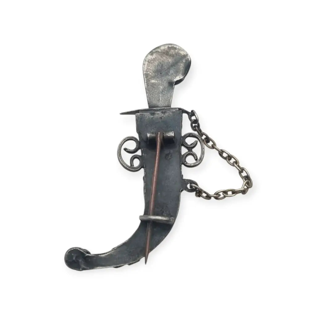 Broche de plata en forma daga con detalles dorados y pedrería colores