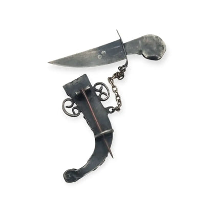 Broche de plata en forma daga con detalles dorados y pedrería colores