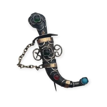 Broche de plata en forma daga con detalles dorados y pedrería colores