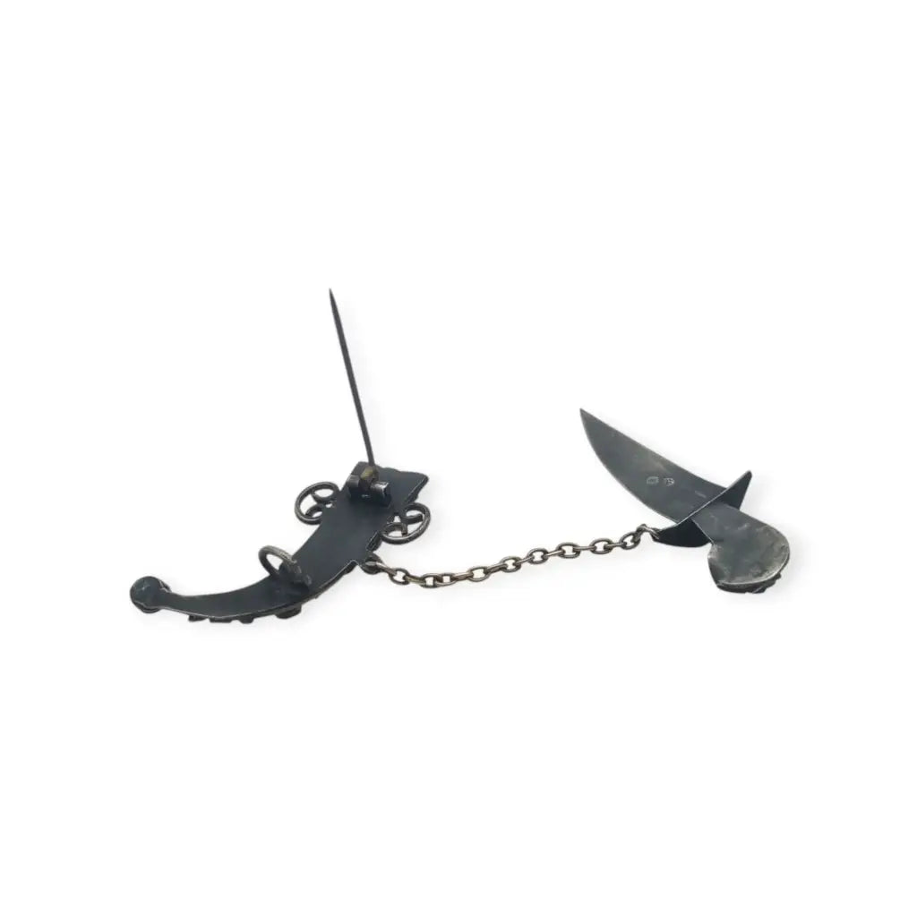 Broche de plata en forma daga con detalles dorados y pedrería colores