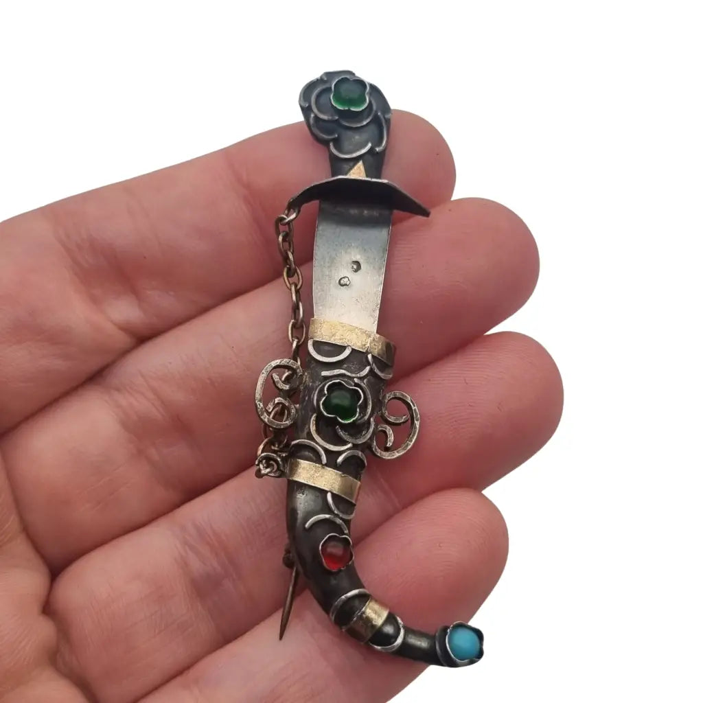 Broche de plata en forma daga con detalles dorados y pedrería colores