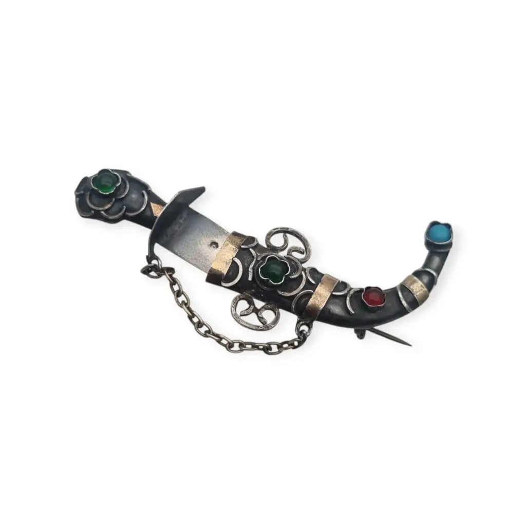 Broche de plata en forma daga con detalles dorados y pedrería colores