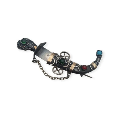 Broche de plata en forma daga con detalles dorados y pedrería colores