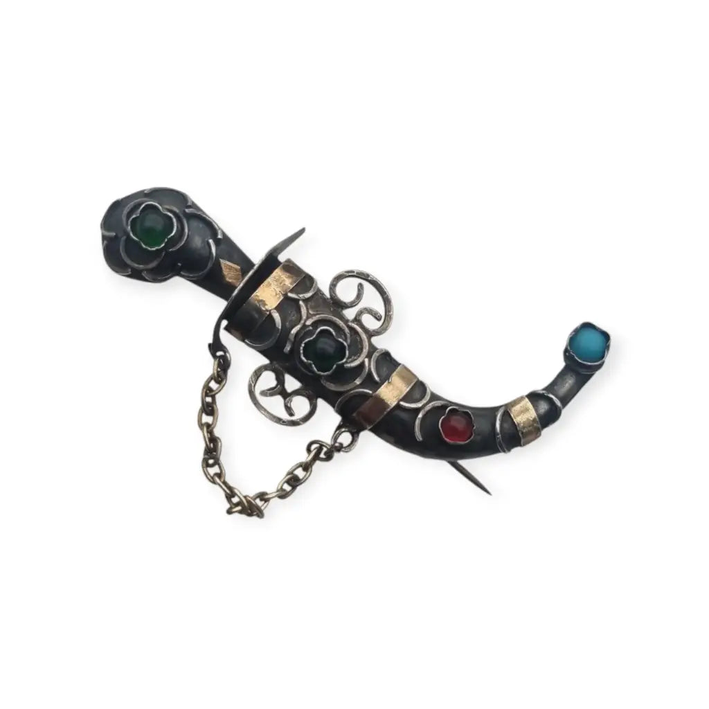 Broche de plata en forma daga con detalles dorados y pedrería colores