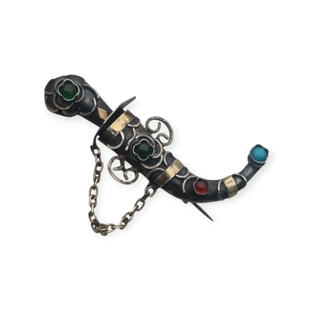 Broche de plata en forma daga con detalles dorados y pedrería colores