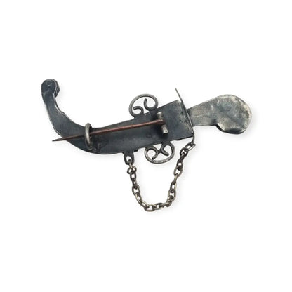 Broche de plata en forma daga con detalles dorados y pedrería colores