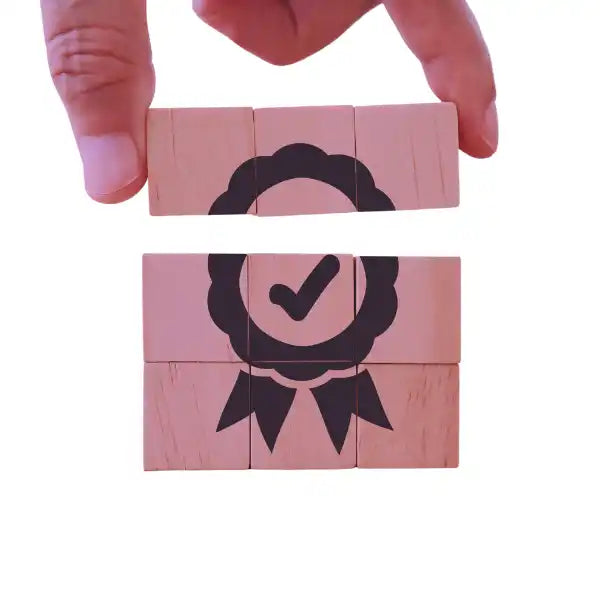 Ícono de premio estilo cinta con una marca de verificación, ensamblado a partir de bloques de madera rosa.